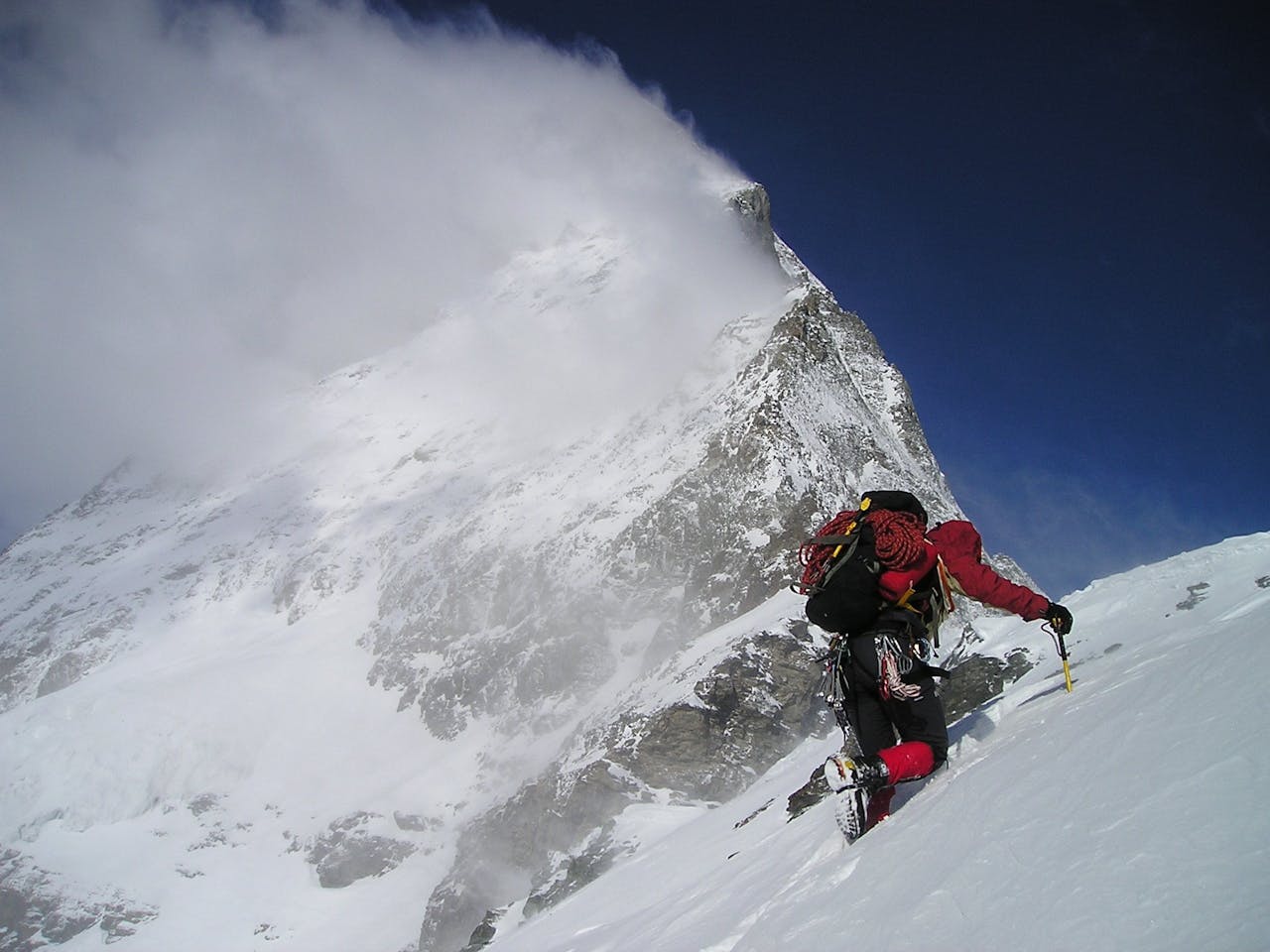 Thrilling adventure of a climber scaling a snowy mountain with dramatic clouds above.