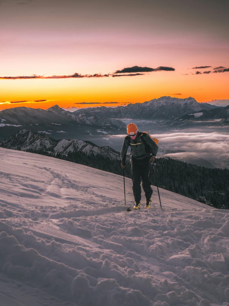 Skier climbs a snowy mountain with breathtaking sunset views, perfect for adventure enthusiasts.